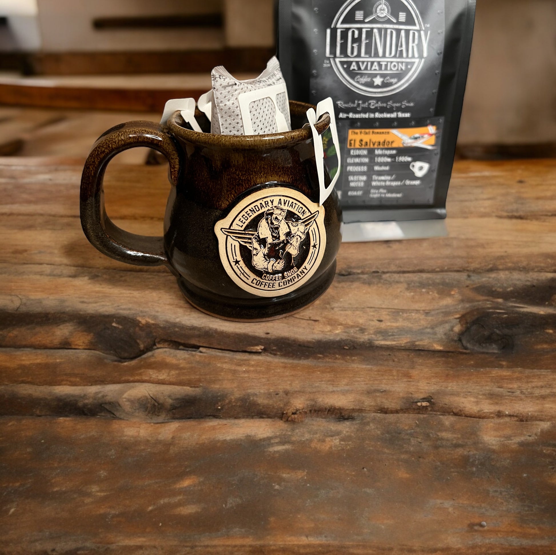 12oz Potbelly Flight Fuel Mug with portable drip filter bag from Legendary Aviation Coffee Company in a cozy coffee shop setting, showcasing its elegant design and handcrafted quality, paired with air-roasted, small batch, single origin, specialty grade boujee coffee roasted in Rockwall, Texas