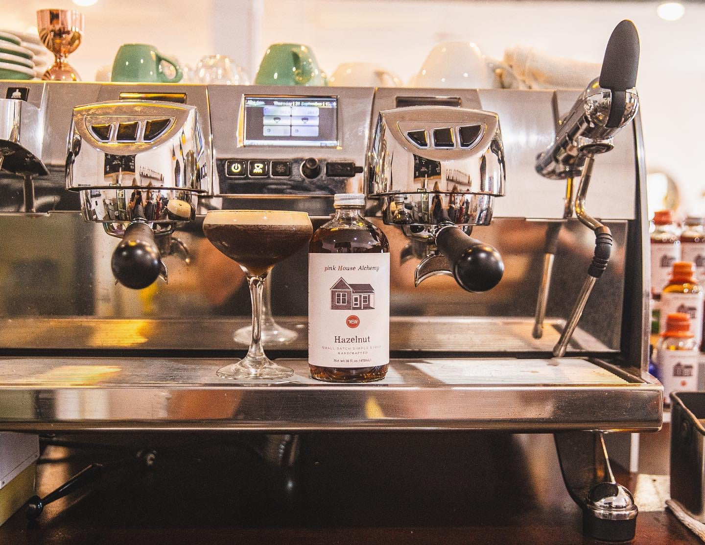 Hazelnut Simple Syrup by Pink House Alchemy next to a specialty coffee mug at Legendary Aviation Coffee in Rockwall, TX – rich, earthy, boujee flavor infusion.